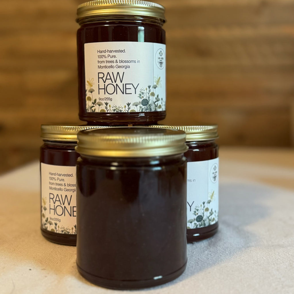 Four jars of raw honey with gold lids on a wooden surface.