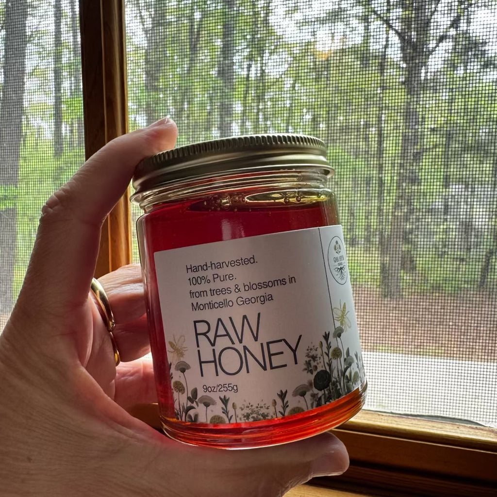 Hand holding a jar of raw honey with a label in front of a window